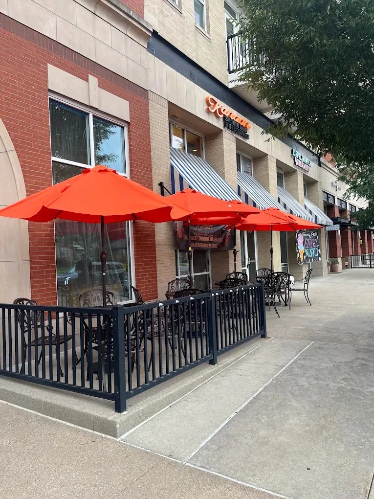 The finished Kanoon patio: red umbrellas over café tables inside a steel railing, with the restaurant’s signage above the storefront glazing.